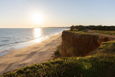 Atlantik 'in sakin sularında, gelgitte yansımaları olan deniz. Praia do Poo Velho, Praia da Falsia, Quarteira, Algarve, Portekiz uçurumlarındaki gün batımının manzarası.