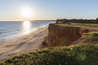 Atlantik 'in sakin sularında, gelgitte yansımaları olan deniz. Praia do Poo Velho, Praia da Falsia, Quarteira, Algarve, Portekiz uçurumlarındaki gün batımının manzarası.