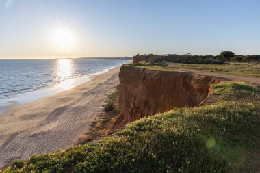 Atlantik 'in sakin sularında, gelgitte yansımaları olan deniz. Praia do Poo Velho, Praia da Falsia, Quarteira, Algarve, Portekiz uçurumlarındaki gün batımının manzarası.