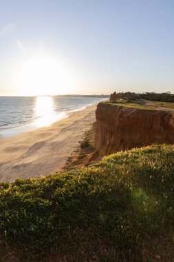 Atlantik 'in sakin sularında, gelgitte yansımaları olan deniz. Praia do Poo Velho, Praia da Falsia, Quarteira, Algarve, Portekiz uçurumlarındaki gün batımının manzarası.