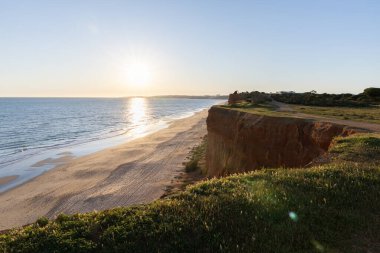 Atlantik 'in sakin sularında, gelgitte yansımaları olan deniz. Praia do Poo Velho, Praia da Falsia, Quarteira, Algarve, Portekiz uçurumlarındaki gün batımının manzarası.