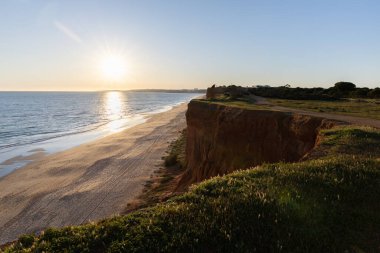 Atlantik 'in sakin sularında, gelgitte yansımaları olan deniz. Praia do Poo Velho, Praia da Falsia, Quarteira, Algarve, Portekiz uçurumlarındaki gün batımının manzarası.