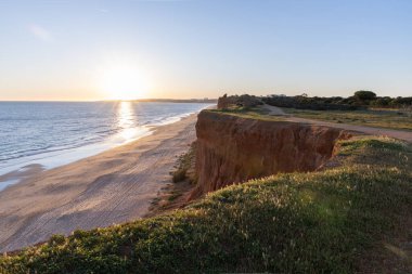 Atlantik 'in sakin sularında, gelgitte yansımaları olan deniz. Praia do Poo Velho, Praia da Falsia, Quarteira, Algarve, Portekiz uçurumlarındaki gün batımının manzarası.