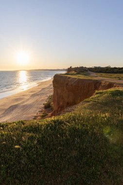 Atlantik 'in sakin sularında, gelgitte yansımaları olan deniz. Praia do Poo Velho, Praia da Falsia, Quarteira, Algarve, Portekiz uçurumlarındaki gün batımının manzarası.