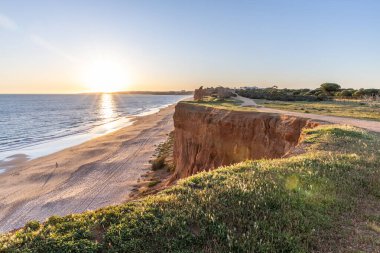 Atlantik 'in sakin sularında, gelgitte yansımaları olan deniz. Praia do Poo Velho, Praia da Falsia, Quarteira, Algarve, Portekiz uçurumlarındaki gün batımının manzarası.