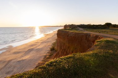 Atlantik 'in sakin sularında, gelgitte yansımaları olan deniz. Praia do Poo Velho, Praia da Falsia, Quarteira, Algarve, Portekiz uçurumlarındaki gün batımının manzarası.