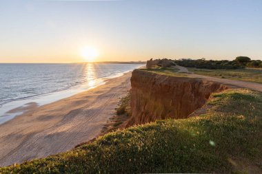 Atlantik 'in sakin sularında, gelgitte yansımaları olan deniz. Praia do Poo Velho, Praia da Falsia, Quarteira, Algarve, Portekiz uçurumlarındaki gün batımının manzarası.