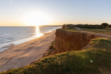 Atlantik 'in sakin sularında, gelgitte yansımaları olan deniz. Praia do Poo Velho, Praia da Falsia, Quarteira, Algarve, Portekiz uçurumlarındaki gün batımının manzarası.