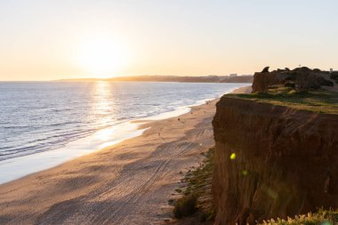 Atlantik 'in sakin sularında, gelgitte yansımaları olan deniz. Praia do Poo Velho, Praia da Falsia, Quarteira, Algarve, Portekiz uçurumlarındaki gün batımının manzarası.
