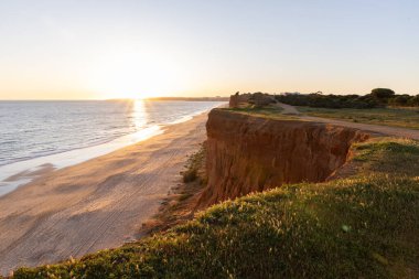 Atlantik 'in sakin sularında, gelgitte yansımaları olan deniz. Praia do Poo Velho, Praia da Falsia, Quarteira, Algarve, Portekiz uçurumlarındaki gün batımının manzarası.