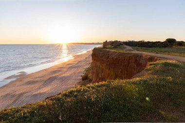 Atlantik 'in sakin sularında, gelgitte yansımaları olan deniz. Praia do Poo Velho, Praia da Falsia, Quarteira, Algarve, Portekiz uçurumlarındaki gün batımının manzarası.
