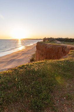 Atlantik 'in sakin sularında, gelgitte yansımaları olan deniz. Praia do Poo Velho, Praia da Falsia, Quarteira, Algarve, Portekiz uçurumlarındaki gün batımının manzarası.