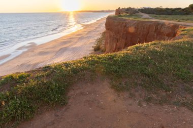 Atlantik 'in sakin sularında, gelgitte yansımaları olan deniz. Praia do Poo Velho, Praia da Falsia, Quarteira, Algarve, Portekiz uçurumlarındaki gün batımının manzarası.