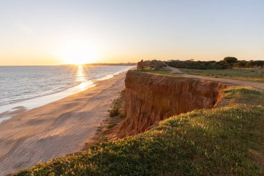 Atlantik 'in sakin sularında, gelgitte yansımaları olan deniz. Praia do Poo Velho, Praia da Falsia, Quarteira, Algarve, Portekiz uçurumlarındaki gün batımının manzarası.