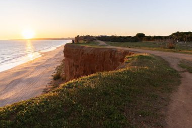 Atlantik 'in sakin sularında, gelgitte yansımaları olan deniz. Praia do Poo Velho, Praia da Falsia, Quarteira, Algarve, Portekiz uçurumlarındaki gün batımının manzarası.