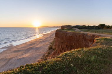 Atlantik 'in sakin sularında, gelgitte yansımaları olan deniz. Praia do Poo Velho, Praia da Falsia, Quarteira, Algarve, Portekiz uçurumlarındaki gün batımının manzarası.