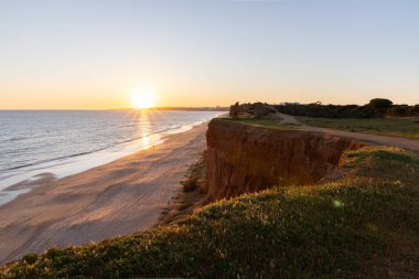 Atlantik 'in sakin sularında, gelgitte yansımaları olan deniz. Praia do Poo Velho, Praia da Falsia, Quarteira, Algarve, Portekiz uçurumlarındaki gün batımının manzarası.