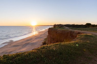 Atlantik 'in sakin sularında, gelgitte yansımaları olan deniz. Praia do Poo Velho, Praia da Falsia, Quarteira, Algarve, Portekiz uçurumlarındaki gün batımının manzarası.