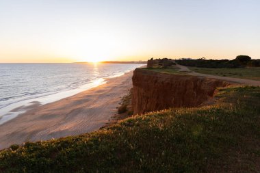 Atlantik 'in sakin sularında, gelgitte yansımaları olan deniz. Praia do Poo Velho, Praia da Falsia, Quarteira, Algarve, Portekiz uçurumlarındaki gün batımının manzarası.