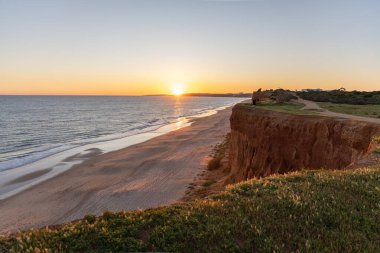 Atlantik 'in sakin sularında, gelgitte yansımaları olan deniz. Praia do Poo Velho, Praia da Falsia, Quarteira, Algarve, Portekiz uçurumlarındaki gün batımının manzarası.