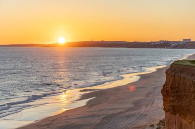 Atlantik 'in sakin sularında, gelgitte yansımaları olan deniz. Praia do Poo Velho, Praia da Falsia, Quarteira, Algarve, Portekiz uçurumlarındaki gün batımının manzarası.