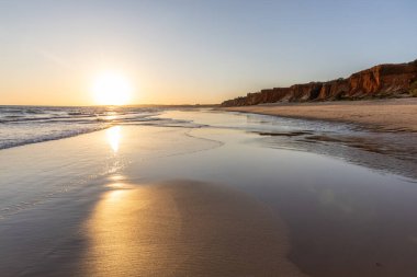 Atlantik 'te kumlu bir sahil. Kum taşı kayalıkları olan bir sahilin gün batımında manzara. Albufeira, Algarve, Portekiz yakınlarındaki Praia da Falsia 'nın sarı sahilinde gelgit var.