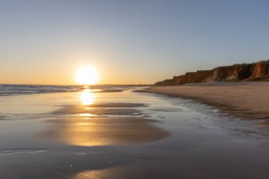 Atlantik 'te kumlu bir sahil. Kum taşı kayalıkları olan bir sahilin gün batımında manzara. Albufeira, Algarve, Portekiz yakınlarındaki Praia da Falsia 'nın sarı sahilinde gelgit var.