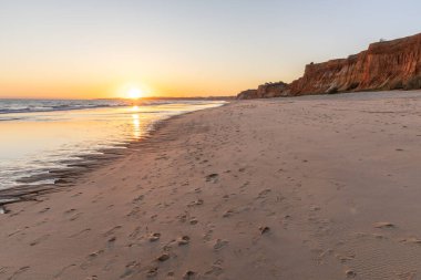 Atlantik 'te kumlu bir sahil. Kum taşı kayalıkları olan bir sahilin gün batımında manzara. Albufeira, Algarve, Portekiz yakınlarındaki Praia da Falsia 'nın sarı sahilinde gelgit var.