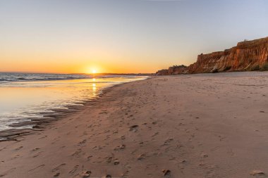 Atlantik 'te kumlu bir sahil. Kum taşı kayalıkları olan bir sahilin gün batımında manzara. Albufeira, Algarve, Portekiz yakınlarındaki Praia da Falsia 'nın sarı sahilinde gelgit var.