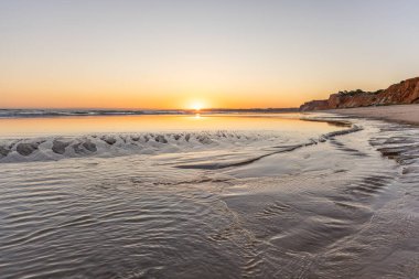 Atlantik 'te kumlu bir sahil. Kum taşı kayalıkları olan bir sahilin gün batımında manzara. Albufeira, Algarve, Portekiz yakınlarındaki Praia da Falsia 'nın sarı sahilinde gelgit var.