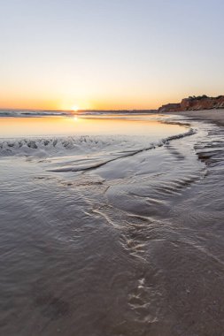 Atlantik 'te kumlu bir sahil. Kum taşı kayalıkları olan bir sahilin gün batımında manzara. Albufeira, Algarve, Portekiz yakınlarındaki Praia da Falsia 'nın sarı sahilinde gelgit var.