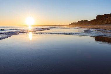 Atlantik 'te kumlu bir sahil. Kum taşı kayalıkları olan bir sahilin gün batımında manzara. Albufeira, Algarve, Portekiz yakınlarındaki Praia da Falsia 'nın sarı sahilinde gelgit var.