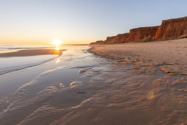 Atlantik 'te kumlu bir sahil. Kum taşı kayalıkları olan bir sahilin gün batımında manzara. Albufeira, Algarve, Portekiz yakınlarındaki Praia da Falsia 'nın sarı sahilinde gelgit var.