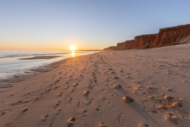 Atlantik 'te kumlu bir sahil. Kum taşı kayalıkları olan bir sahilin gün batımında manzara. Albufeira, Algarve, Portekiz yakınlarındaki Praia da Falsia 'nın sarı sahilinde gelgit var.