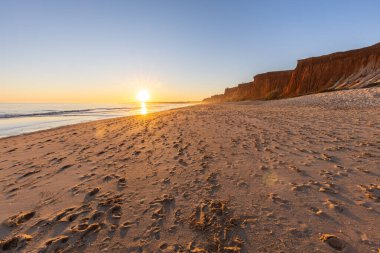 Atlantik 'te kumlu bir sahil. Kum taşı kayalıkları olan bir sahilin gün batımında manzara. Albufeira, Algarve, Portekiz yakınlarındaki Praia da Falsia 'nın sarı sahilinde gelgit var.