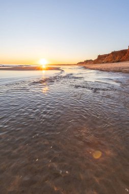 Atlantik 'te kumlu bir sahil. Kum taşı kayalıkları olan bir sahilin gün batımında manzara. Albufeira, Algarve, Portekiz yakınlarındaki Praia da Falsia 'nın sarı sahilinde gelgit var.