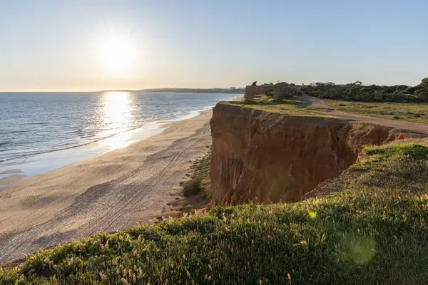 Atlantik 'in sakin sularında, gelgitte yansımaları olan deniz. Praia do Poo Velho, Praia da Falsia, Quarteira, Algarve, Portekiz uçurumlarındaki gün batımının manzarası.