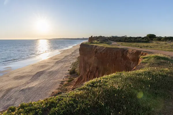 Atlantik 'in sakin sularında, gelgitte yansımaları olan deniz. Praia do Poo Velho, Praia da Falsia, Quarteira, Algarve, Portekiz uçurumlarındaki gün batımının manzarası.