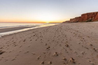 Atlantik 'te kumlu bir sahil. Kum taşı kayalıkları olan bir sahilin gün batımında manzara. Albufeira, Algarve, Portekiz yakınlarındaki Praia da Falsia 'nın sarı sahilinde gelgit var.