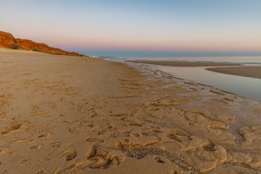 Atlantik 'te kumlu bir sahil. Kum taşı kayalıkları olan bir sahilin gün batımında manzara. Albufeira, Algarve, Portekiz yakınlarındaki Praia da Falsia 'nın sarı sahilinde gelgit var.
