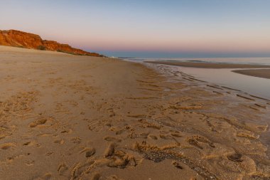 Atlantik 'te kumlu bir sahil. Kum taşı kayalıkları olan bir sahilin gün batımında manzara. Albufeira, Algarve, Portekiz yakınlarındaki Praia da Falsia 'nın sarı sahilinde gelgit var.