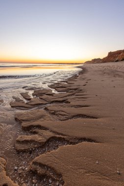 Atlantik 'te kumlu bir sahil. Kum taşı kayalıkları olan bir sahilin gün batımında manzara. Albufeira, Algarve, Portekiz yakınlarındaki Praia da Falsia 'nın sarı sahilinde gelgit var.