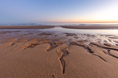Atlantik 'te kumlu bir sahil. Kum taşı kayalıkları olan bir sahilin gün batımında manzara. Albufeira, Algarve, Portekiz yakınlarındaki Praia da Falsia 'nın sarı sahilinde gelgit var.