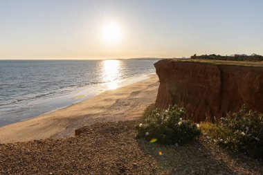 Atlantik 'in sakin sularında, gelgitte yansımaları olan deniz. Praia do Poo Velho, Praia da Falsia, Quarteira, Algarve, Portekiz uçurumlarındaki gün batımının manzarası.