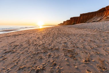 Atlantik 'te kumlu bir sahil. Kum taşı kayalıkları olan bir sahilin gün batımında manzara. Albufeira, Algarve, Portekiz yakınlarındaki Praia da Falsia 'nın sarı sahilinde gelgit var.