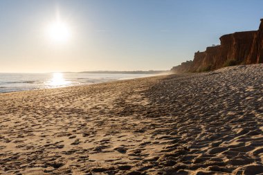 Atlantik 'te kumlu bir sahil. Kum taşı kayalıkları olan bir sahilin gün batımında manzara. Albufeira, Algarve, Portekiz yakınlarındaki Praia da Falsia 'nın sarı sahilinde gelgit var.