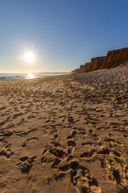 Atlantik 'te kumlu bir sahil. Kum taşı kayalıkları olan bir sahilin gün batımında manzara. Albufeira, Algarve, Portekiz yakınlarındaki Praia da Falsia 'nın sarı sahilinde gelgit var.