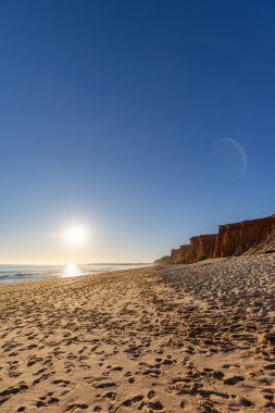 Atlantik 'te kumlu bir sahil. Kum taşı kayalıkları olan bir sahilin gün batımında manzara. Albufeira, Algarve, Portekiz yakınlarındaki Praia da Falsia 'nın sarı sahilinde gelgit var.