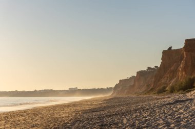 Atlantik 'te kumlu bir sahil. Kum taşı kayalıkları olan bir sahilin gün batımında manzara. Albufeira, Algarve, Portekiz yakınlarındaki Praia da Falsia 'nın sarı sahilinde gelgit var.