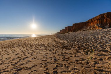 Atlantik 'te kumlu bir sahil. Kum taşı kayalıkları olan bir sahilin gün batımında manzara. Albufeira, Algarve, Portekiz yakınlarındaki Praia da Falsia 'nın sarı sahilinde gelgit var.